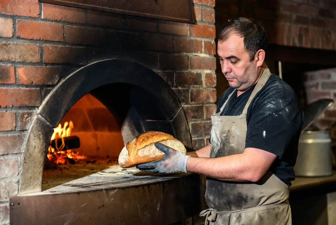 Baker pulling a crusty sourdough loaf from a wood-fired oven in an independent bakery